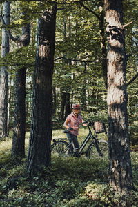 Man sitting on bicycle by tree trunks in forest