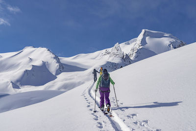 Rear view of people skiing on snowcapped mountain against sky