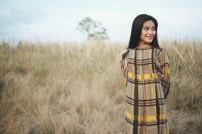 Portrait of smiling young woman standing on field against sky