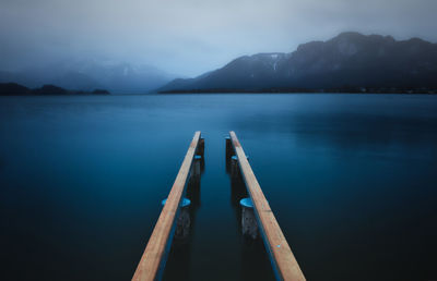 Wooden posts in lake against sky