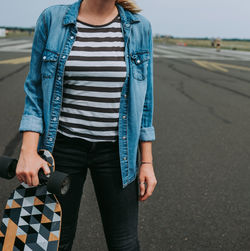 Midsection of woman holding skateboard while standing on road