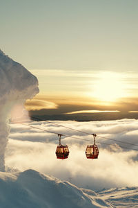 Ski lifts above clouds at sunset