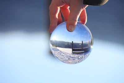 Close-up of cropped hand holding crystal ball with reflection during winter