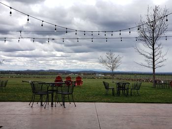 Empty chairs and table on field against sky