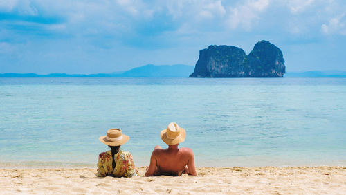 Rear view of woman sitting at beach against sky