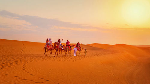 People on sand dune in desert against sky