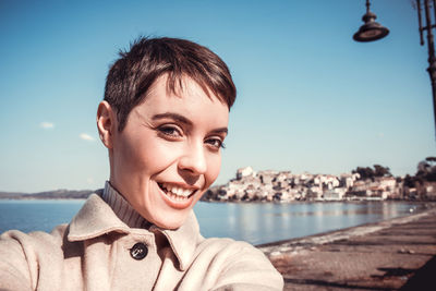 Beautiful young woman with short hair is taking a selfie in front of the lake.
