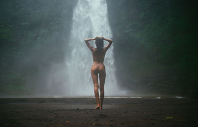 Full length of woman standing against waterfall