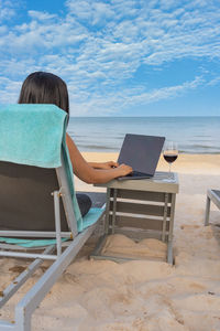 Low section of woman using laptop at beach