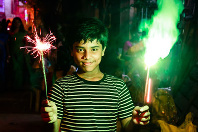 Portrait of teenage boy holding sparklers at night