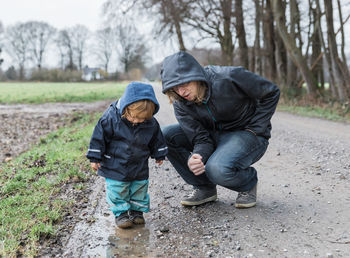 Father crouching by baby girl standing on puddle