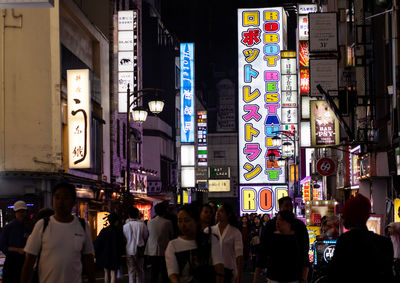 People walking on illuminated street in city at night