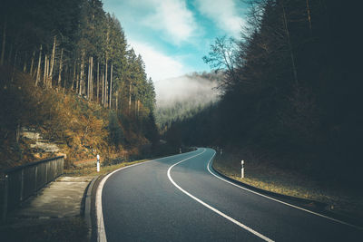 Empty road amidst trees against sky