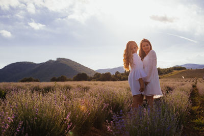 Portrait of cheerful sisters standing on field against sky