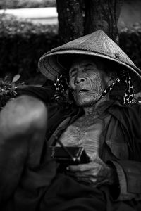 Senior man wearing asian style conical hat while napping outdoors with radio