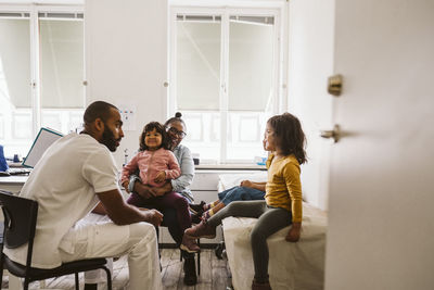 Smiling mother and daughter looking at male doctor consulting girls at medical clinic
