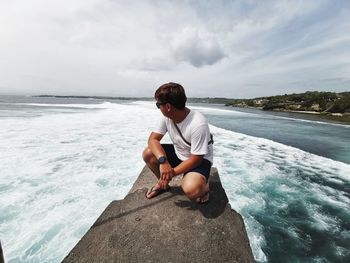 Woman sitting on rock looking at sea against sky