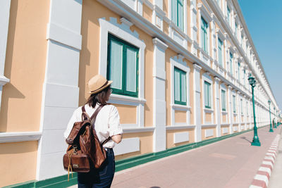 Behind of young asian woman with backpack and straw hat travel in old town bangkok, thailand