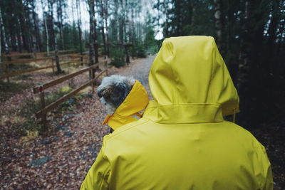 Rear view of person wearing yellow raincoat while carrying dog in forest