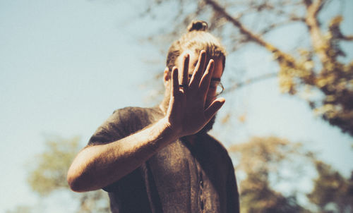 Man showing stop gesture over face against trees and sky