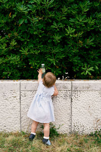 Rear view of girl reaching to bottle on wall