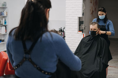 Female barber wearing mask cutting hair of customer