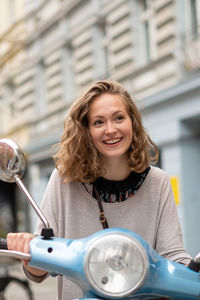 Smiling woman standing on motorcycle outdoors