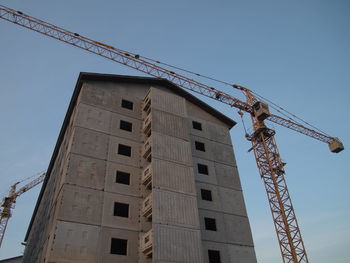 Low angle view of crane by building against sky