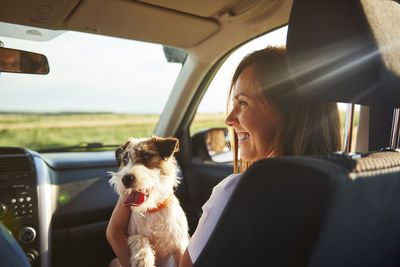 Smiling woman with dog sitting in car