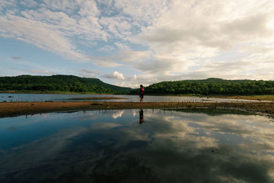 Reflection of woman standing on water against sky
