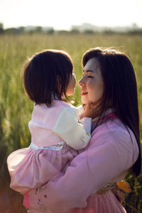 Korean woman with daughter child, stands on a green field at sunset in summer in national costumes