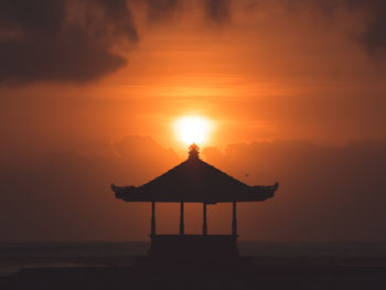 Silhouette temple building by sea against sky during sunset
