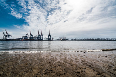 Cranes at commercial dock against sky