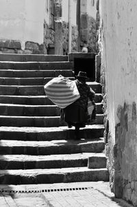 Rear view of senior woman carrying burden while moving up on steps