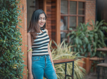 Portrait of smiling young woman standing against plants