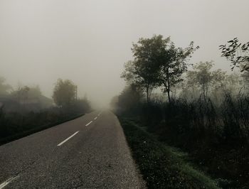 Road amidst trees against sky during foggy weather