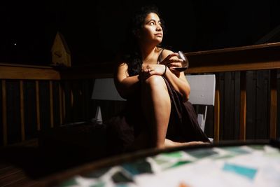 Thoughtful young woman with wineglass sitting at balcony during night