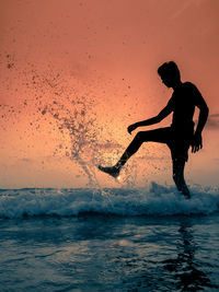 Silhouette man surfing in sea against sky during sunset