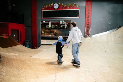 Back on skateboard instructor holding hands with student while skating