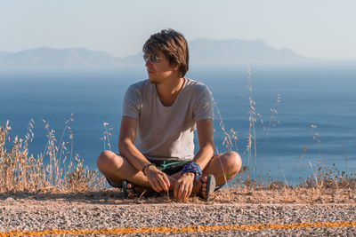 Full length of young man sitting on mountain against sky