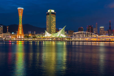 Illuminated city by river against sky at night