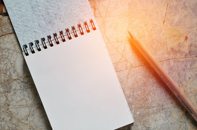 Close-up of open notebook and pencil on cracked floor