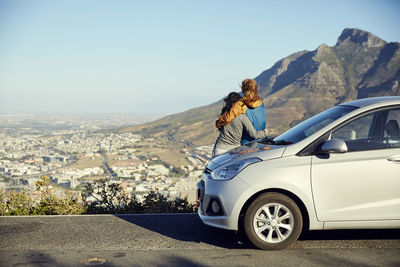 South africa, cape town, signal hill, two young women leaning against car overlooking the city