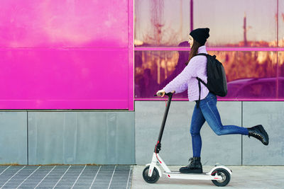 Side view of woman with pink umbrella against wall