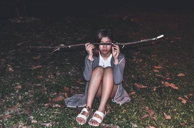 High angle view of teenage girl holding twig while sitting on field at night