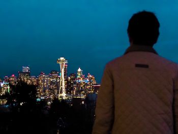 Rear view of man looking at illuminated city buildings during night