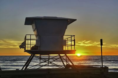 Lifeguard hut on beach against sky during sunset