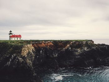 Lighthouse on sea against cloudy sky