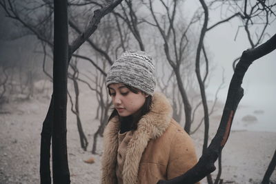 Portrait of young woman with bare tree in winter