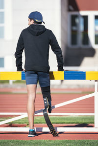 Rear view of athlete with prosthetic leg while standing by railing